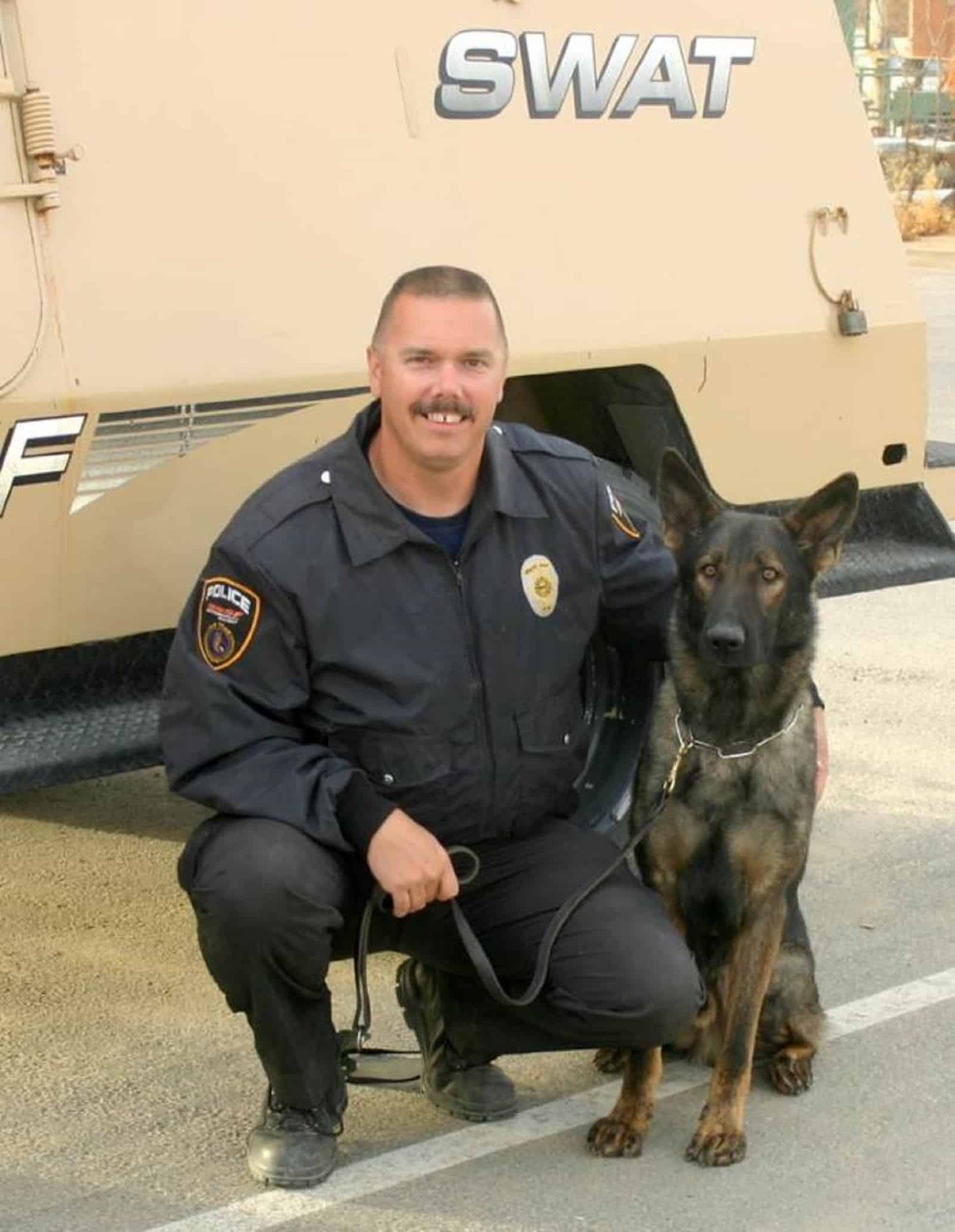 police officer embracing his dog sitting beside him